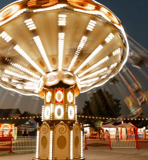 Blurred motion of an illuminated chain swing ride at a carnival during dusk.